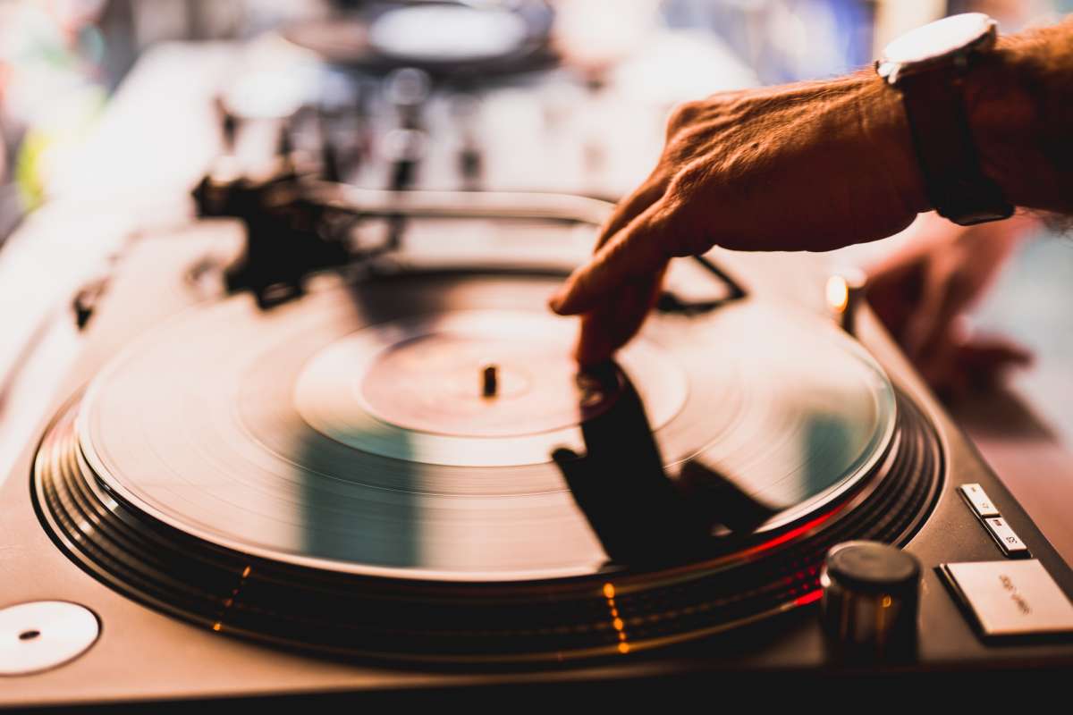 Dj hands on equipment deck and mixer with vinyl record at party